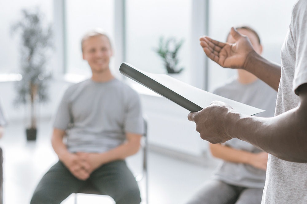 man with notebook addressing support group for men