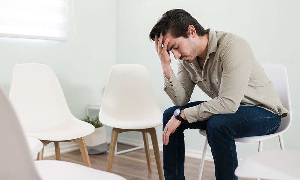 man sitting alone in a circle of empty chairs