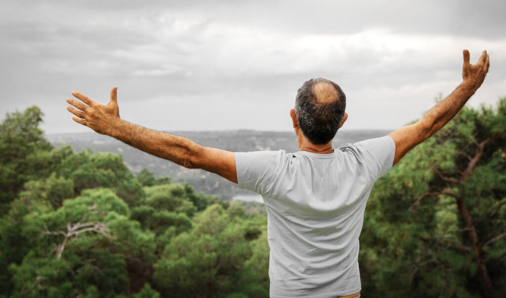 man standing in the mountains and stretching his arms open and above his head